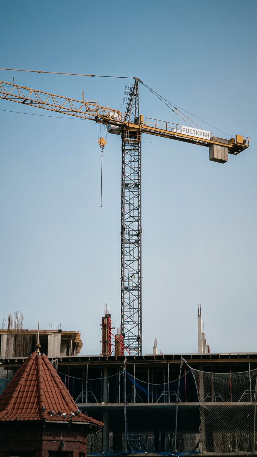 Grúa amarilla trabajando sobre una obra con un tejado de teja en primer plano